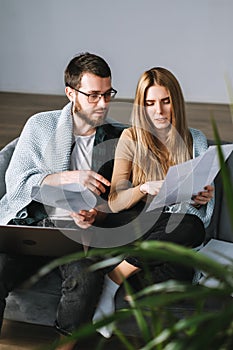 Young couple manages finances with laptop, looking through their bank accounts in the living room on the sofa