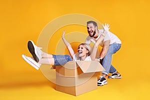 Young couple in matching outfits having fun moving boxes, isolated on yellow