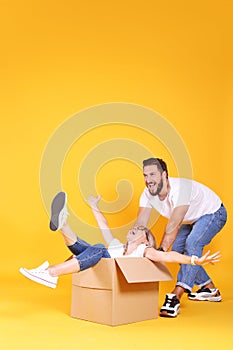 Young couple in matching outfits having fun moving boxes, isolated on yellow
