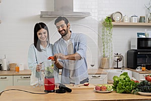 Young couple mixing fruit in a food processor, making a smoothie. Husband and wife having fun with smoothie in the kitchen and