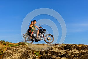 Young couple on a motorcycle on on rocky ground. Happy guy and girl travelling on a motorbike