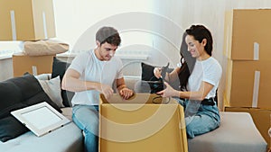 Young couple move into new apartment. Camera moves to right where man and woman sitting and unpacking box with stuff