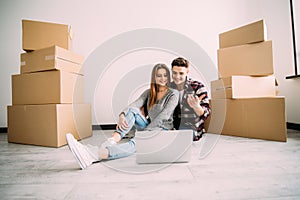 Young couple moving in a new home. Man and woman with notebook laptop computer and boxes in empty room.