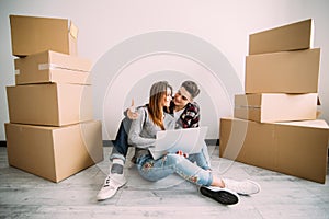 Young couple moving in a new home. Man and woman with notebook laptop computer and boxes in empty room.