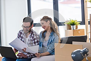 Young couple moving in new home. Sitting and relaxing after unpacking. Looking something on laptop