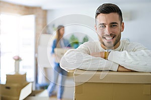 Young couple moving to a new home, handsome man smiling leaning on cardboard boxes