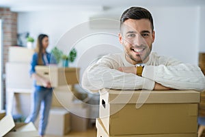 Young couple moving to a new home, handsome man smiling leaning on cardboard boxes