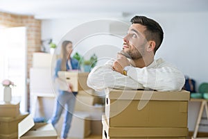 Young couple moving to a new home, handsome man smiling leaning on cardboard boxes