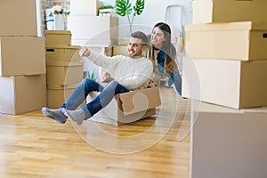 Young couple moving to a new home, having fun riding cardboard boxes