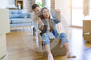 Young couple moving to a new home, having fun riding cardboard boxes