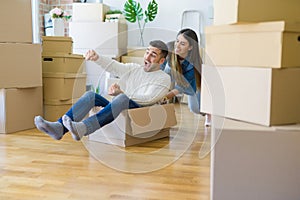 Young couple moving to a new home, having fun riding cardboard boxes