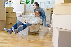 Young couple moving to a new home, having fun riding cardboard boxes