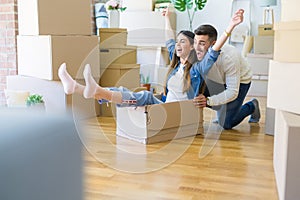 Young couple moving to a new home, having fun riding cardboard boxes