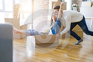 Young couple moving to a new home, having fun riding cardboard boxes