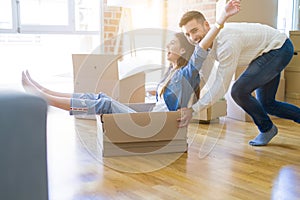 Young couple moving to a new home, having fun riding cardboard boxes