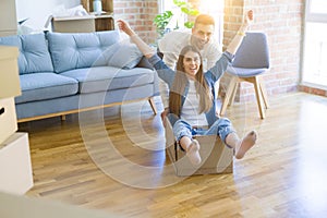 Young couple moving to a new home, having fun riding cardboard boxes