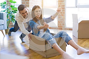 Young couple moving to a new home, having fun riding cardboard boxes