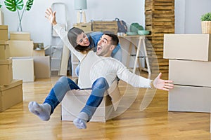 Young couple moving to a new home, having fun riding cardboard boxes