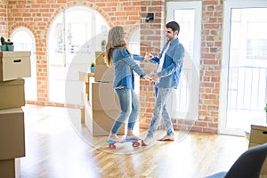 Young couple moving to a new home, having fun riding a skateboard at new apartment around cardboard boxes
