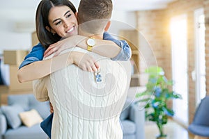 Young couple moving to a new home, hugging in love showing keys of new apartment smiling very happy