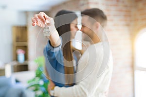 Young couple moving to a new home, hugging in love showing keys of new apartment smiling very happy