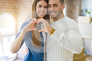 Young couple moving to a new home, hugging in love showing keys of new apartment smiling very happy