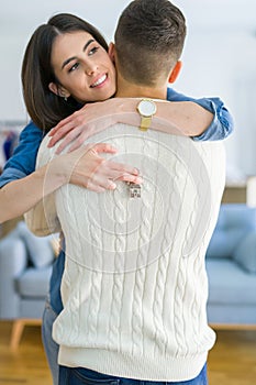 Young couple moving to a new home, hugging in love showing keys of new apartment smiling very happy