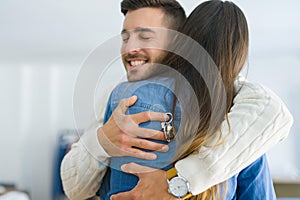 Young couple moving to a new home, hugging in love showing keys of new apartment smiling very happy