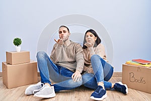 Young couple moving to a new home looking at the camera blowing a kiss with hand on air being lovely and sexy