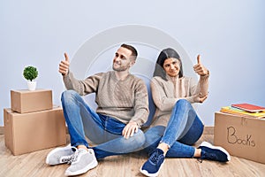 Young couple moving to a new home looking proud, smiling doing thumbs up gesture to the side