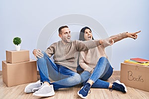 Young couple moving to a new home pointing with finger surprised ahead, open mouth amazed expression, something on the front
