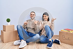 Young couple moving to a new home pointing to the back behind with hand and thumbs up, smiling confident