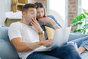 Young couple moving to a new home relaxing sitting on the sofa using computer laptop, smiling happy for moving to new apartment