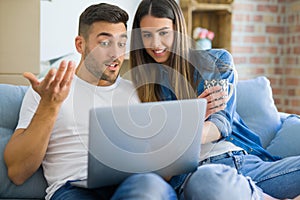 Young couple moving to a new home relaxing sitting on the sofa using computer laptop, smiling happy for moving to new apartment