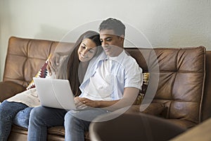 Young couple moving to a new home relaxing sitting on the sofa using computer laptop, smiling happy for moving to new apartment