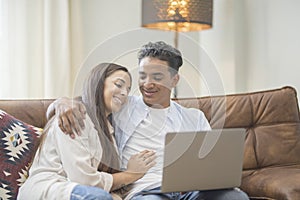 Young couple moving to a new home relaxing sitting on the sofa using computer laptop, smiling happy for moving to new apartment