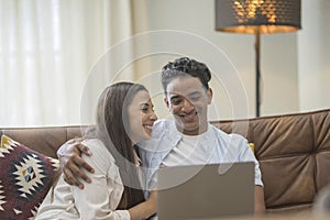 Young couple moving to a new home relaxing sitting on the sofa using computer laptop, smiling happy for moving to new apartment