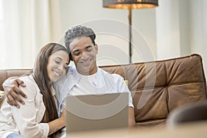 Young couple moving to a new home relaxing sitting on the sofa using computer laptop, smiling happy for moving to new apartment