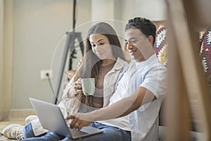 Young couple moving to a new home relaxing sitting on the sofa using computer laptop, smiling happy for moving to new apartment