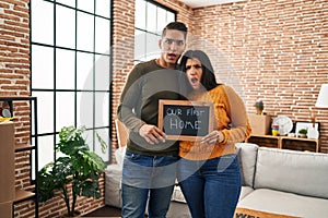 Young couple moving to a new home in shock face, looking skeptical and sarcastic, surprised with open mouth