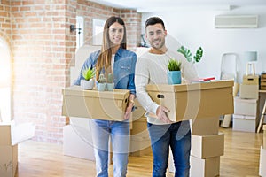 Young couple moving to a new home, smiling happy holding cardboard boxes at new apartment