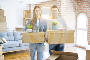 Young couple moving to a new home, smiling happy holding cardboard boxes at new apartment