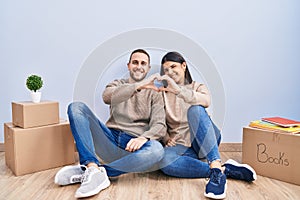 Young couple moving to a new home smiling in love doing heart symbol shape with hands