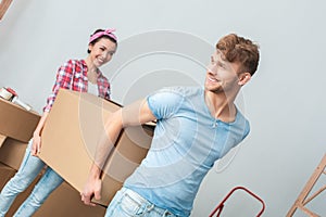 Young couple moving to new place carrying box together talking smiling dreamful