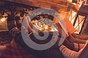 Young couple near the fireplace at home winter reading book and drinking cocoa