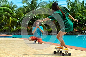 Young couple near swimming pool. Sexy woman with fit body riding on skateboards, and her boyfriend taking photo