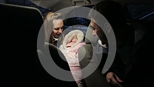 Young couple with a newborn baby sitting in a car and talking.