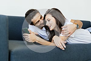 Young couple obsessed with smartphones checking social networks at home using phone apps relaxing together on sofa lost in news