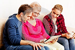 Young couple with old woman sitting on couch and watching something on tablet