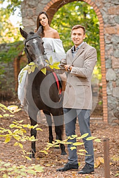 Young couple in the park. The girl is sitting on a horse and the guy is standing side by side.